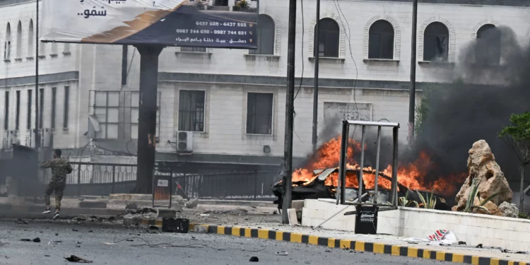 Un miembro del personal de seguridad llega al lugar de los hechos, cerca de un vehículo en llamas, tras una explosión en Damasco el 19 de mayo de 2026. (AFP)