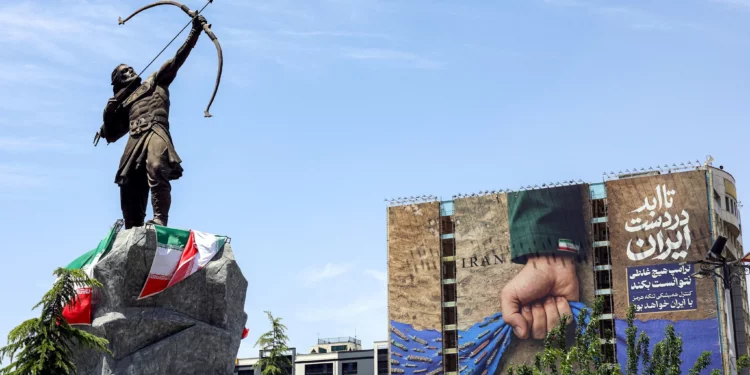 Una estatua que representa a Arash el Arquero, figura mítica persa que según la tradición delimitaba la frontera entre Persia y los turanios, se exhibe cerca de una valla publicitaria en la fachada de un edificio que representa el estrecho de Ormuz con la inscripción en persa “Siempre en manos de Irán”, en la plaza Vanak de Teherán, el 6 de mayo de 2026. (Foto: AFP)