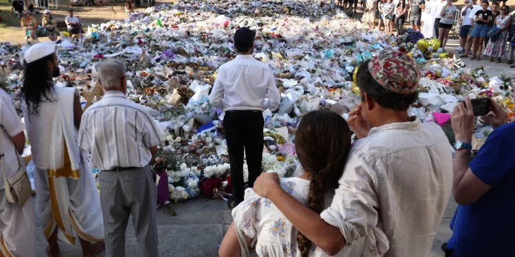 Un rabino (en el centro) pronuncia un sermón mientras los dolientes se reúnen frente a los homenajes depositados en memoria de las víctimas del atentado terrorista perpetrado durante una celebración de Jánuca en Bondi Beach, Sídney, el 20 de diciembre de 2025. (David Gray/AFP)