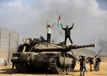 Habitantes de Gaza celebran junto a un tanque israelí destruido en la valla fronteriza rota entre Israel y Gaza, al este de Jan Yunis, el 7 de octubre de 2023. (AP/Yousef Masoud)