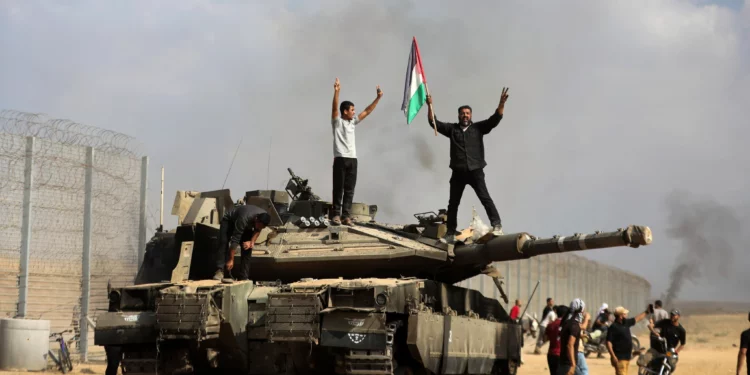 Habitantes de Gaza celebran junto a un tanque israelí destruido en la valla fronteriza rota entre Israel y Gaza, al este de Jan Yunis, el 7 de octubre de 2023. (AP/Yousef Masoud)