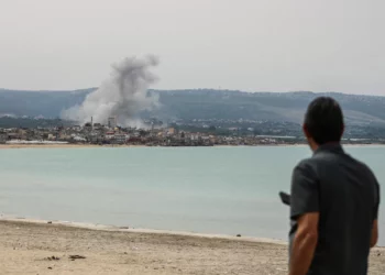 Un hombre de pie en la playa en la zona de Tiro observa el humo que se eleva desde el lugar de un ataque aéreo israelí en la zona de Ras Al-Ain el 12 de mayo de 2026. (KAWNAT HAJU / AFP)