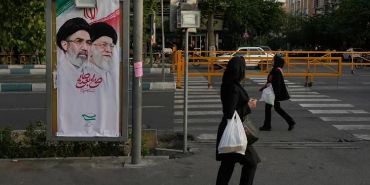 Mujeres caminan junto a una pancarta con retratos del líder supremo iraní, el ayatolá Mojtaba Jamenei (izquierda), y su padre, el asesinado líder supremo, el ayatolá Alí Jamenei, en Teherán, Irán, el 12 de mayo de 2026. (Foto AP/Vahid Salemi)