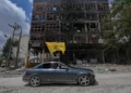 Un hombre con una bandera de Hezbolá pasa en coche junto a un edificio dañado tras el alto el fuego entre Israel y Hezbolá en la localidad de Nabatiyeh, en el sur del Líbano, el 22 de junio de 2026. (Foto AP/Mohammed Zaatari)
