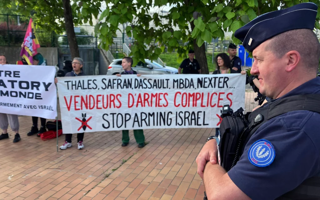 Manifestantes se concentran frente al recinto ferial de Eurosatory, un evento internacional dedicado a la defensa y la seguridad, en Villepinte, a las afueras de París, el 17 de junio de 2024. Un tribunal francés ha prohibido la participación de expositores israelíes; en la pancarta se lee: «Cómplices de los traficantes de armas». (Foto AP/Masha Macpherson)