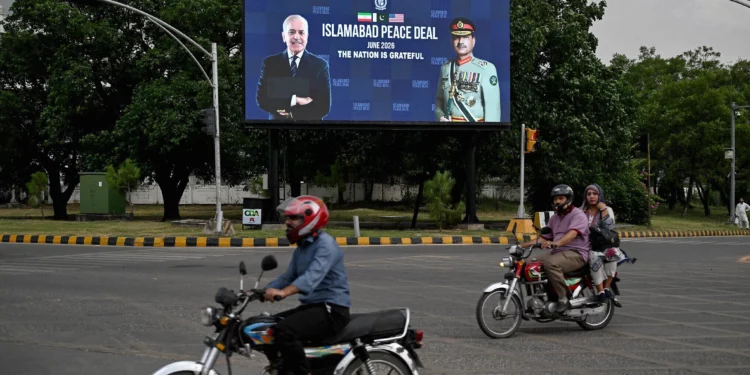Los viajeros pasan junto a un panel electrónico que muestra al primer ministro de Pakistán, Shehbaz Sharif (izquierda), con el jefe del ejército y mariscal de campo Syed Asim Munir, exhibido a lo largo de una carretera en Islamabad el 17 de junio de 2026 (Aamir QURESHI / AFP).