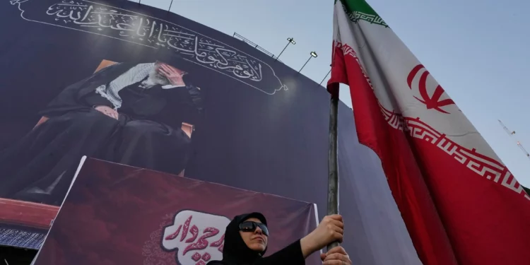 Una mujer partidaria del Gobierno sostiene una bandera iraní bajo una pancarta en la que aparece un retrato del líder supremo asesinado, el ayatolá Alí Jamenei, en una plaza del centro de Teherán, Irán, el 30 de junio de 2026. (Foto AP/Vahid Salemi)