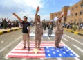 Varios hombres gesticulan mientras expresan su afiliación y apoyo a los islamistas hutíes, de pie junto a una representación de la bandera estadounidense, durante una manifestación de estudiantes universitarios en medio de la escalada de tensiones con Arabia Saudita, en el campus de la Universidad de Sanaa, capital de Yemen controlada por los hutíes, el 22 de julio de 2026. (Mohammed HUWAIS/AFP)