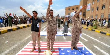 Varios hombres gesticulan mientras expresan su afiliación y apoyo a los islamistas hutíes, de pie junto a una representación de la bandera estadounidense, durante una manifestación de estudiantes universitarios en medio de la escalada de tensiones con Arabia Saudita, en el campus de la Universidad de Sanaa, capital de Yemen controlada por los hutíes, el 22 de julio de 2026. (Mohammed HUWAIS/AFP)