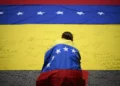 Imagen ilustrativa: Un sindicalista, envuelto en una bandera venezolana, firma otra bandera venezolana durante una marcha en Caracas el 28 de julio de 2026. (Federico PARRA/AFP)
