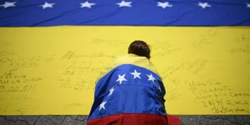 Imagen ilustrativa: Un sindicalista, envuelto en una bandera venezolana, firma otra bandera venezolana durante una marcha en Caracas el 28 de julio de 2026. (Federico PARRA/AFP)