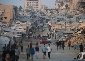 Palestinos caminan junto a tiendas de campaña y edificios destruidos cerca de la playa en la ciudad de Gaza el 14 de agosto de 2026. (Eyad Baba/AFP)