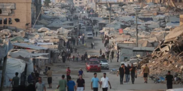 Palestinos caminan junto a tiendas de campaña y edificios destruidos cerca de la playa en la ciudad de Gaza el 14 de agosto de 2026. (Eyad Baba/AFP)