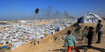 ARCHIVO) Unos niños hacen volar una cometa con el humo que se eleva del refugio de Gath, que alberga a palestinos desplazados, tras un ataque aéreo israelí en el oeste de Jan Yunis, en el sur de la Franja de Gaza, el 31 de enero de 2026. (Bashar Taleb/AFP)