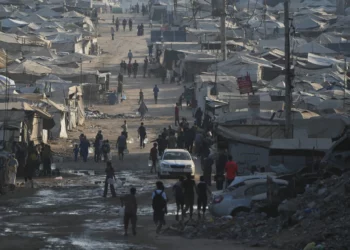 Palestinos caminan entre tiendas de campaña y escombros de edificios destruidos durante la guerra entre Israel y Hamás a lo largo de la carretera costera en la ciudad de Gaza, el 13 de agosto de 2026. (Foto AP/Abdel Kareem Hana)