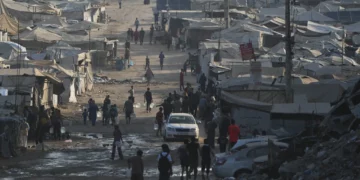 Palestinos caminan entre tiendas de campaña y escombros de edificios destruidos durante la guerra entre Israel y Hamás a lo largo de la carretera costera en la ciudad de Gaza, el 13 de agosto de 2026. (Foto AP/Abdel Kareem Hana)