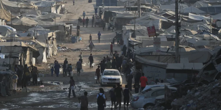 Palestinos caminan entre tiendas de campaña y escombros de edificios destruidos durante la guerra entre Israel y Hamás a lo largo de la carretera costera en la ciudad de Gaza, el 13 de agosto de 2026. (Foto AP/Abdel Kareem Hana)