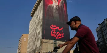 Un hombre pasa en su motocicleta junto a una valla publicitaria con un mensaje en persa que dice: “Debemos levantarnos” y una imagen del difunto líder supremo iraní, el ayatolá Alí Jamenei, en Teherán, Irán, el 15 de agosto de 2026. (AP/Vahid Salemi)