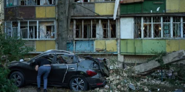 Un residente local observa el interior de un automóvil destruido junto a edificios residenciales gravemente dañados tras un ataque ruso ocurrido durante la noche en Kiev, Ucrania, el 20 de agosto de 2026. (Foto AP/Francisco Seco)