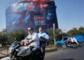 Motociclistas pasan junto a un cartel con Donald Trump bajo el agua y explosiones en Teherán, el 24 de agosto de 2026.