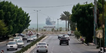 El tráfico circula por una avenida mientras un buque mercante permanece anclado en el estrecho de Ormuz frente a Bandar Abbas, Irán, el 7 de septiembre de 2026.