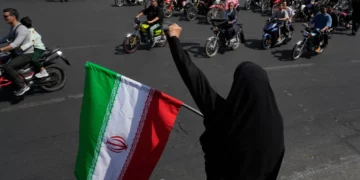 Una mujer sostiene una bandera iraní y corea consignas durante un desfile estatal de motocicletas en Teherán, el 25 de septiembre de 2026.