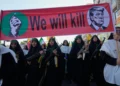 Mujeres vinculadas a la Guardia Revolucionaria de Irán portan rifles durante una marcha en Teherán, bajo una pancarta con Donald Trump en una mira.