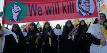 Mujeres vinculadas a la Guardia Revolucionaria de Irán portan rifles durante una marcha en Teherán, bajo una pancarta con Donald Trump en una mira.