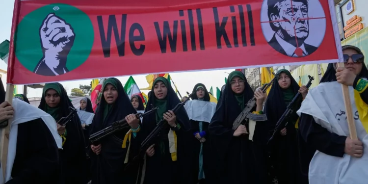 Mujeres vinculadas a la Guardia Revolucionaria de Irán portan rifles durante una marcha en Teherán, bajo una pancarta con Donald Trump en una mira.