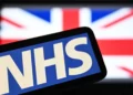 El logotipo del Servicio Nacional de Salud británico (NHS) aparece en una pantalla con la bandera del Reino Unido al fondo, el 7 de julio de 2024.
