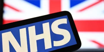 El logotipo del Servicio Nacional de Salud británico (NHS) aparece en una pantalla con la bandera del Reino Unido al fondo, el 7 de julio de 2024.