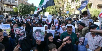 Sirios agitan banderas y muestran retratos de personas presuntamente detenidas durante incursiones militares israelíes en el sur de Siria, durante una protesta cerca del edificio de la ONU en Damasco el 23 de octubre de 2026.