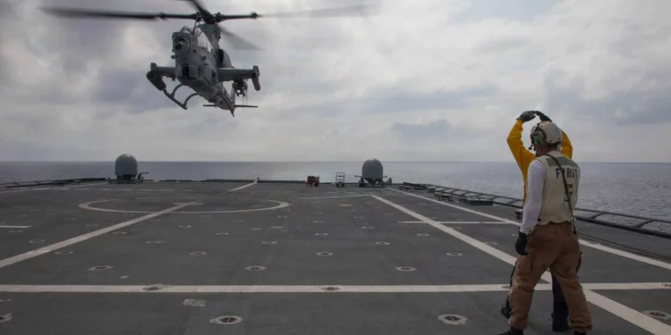 Marineros de la Armada de Estados Unidos señalan a un AH-1Z Viper del HMLA-367 durante su despegue desde la cubierta del USS Canberra en el mar de Filipinas.
